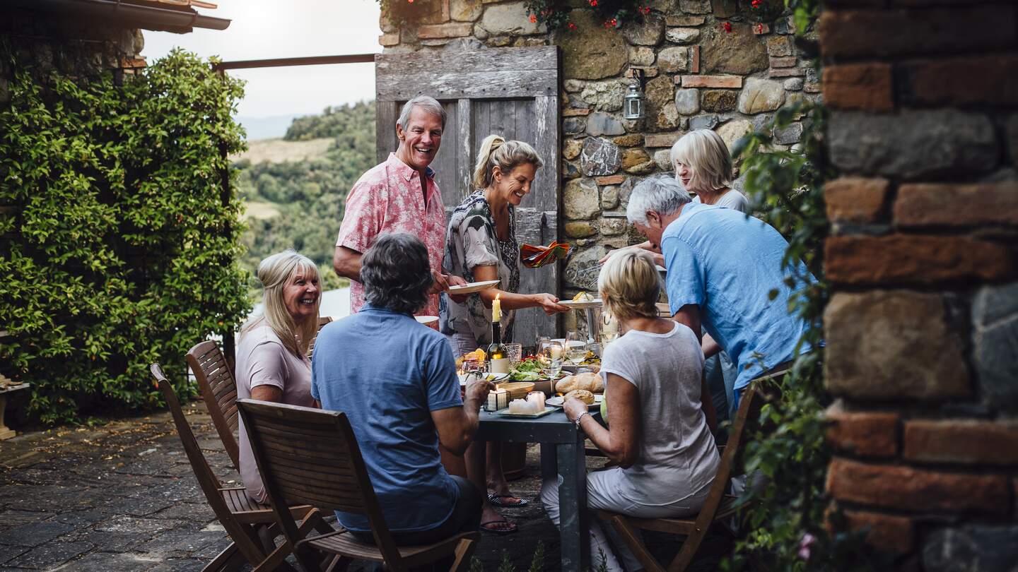 Eine Gruppe reifer Freunde sitzt um einen Esstisch im Freien | © gettyimages.com/SolStock