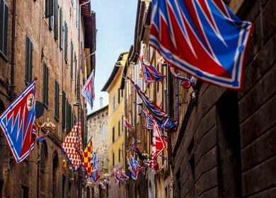 Flaggen der Kontrahenten des jaehrlichen Pferderennens Palio de Siena in der Innenstadt von Siena | © Gettyimages.com/SimoneN