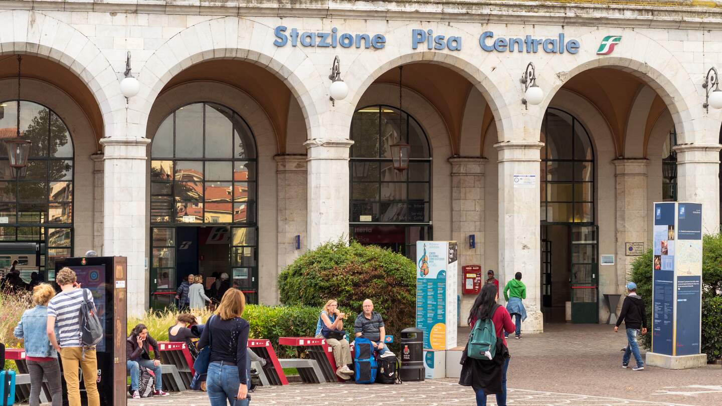 Aussenansicht des Bahnhofs von Pisa mit Arkaden und Menschen auf dem Bahnhofsvorplatz | © Gettyimages.com/George georgecklerk