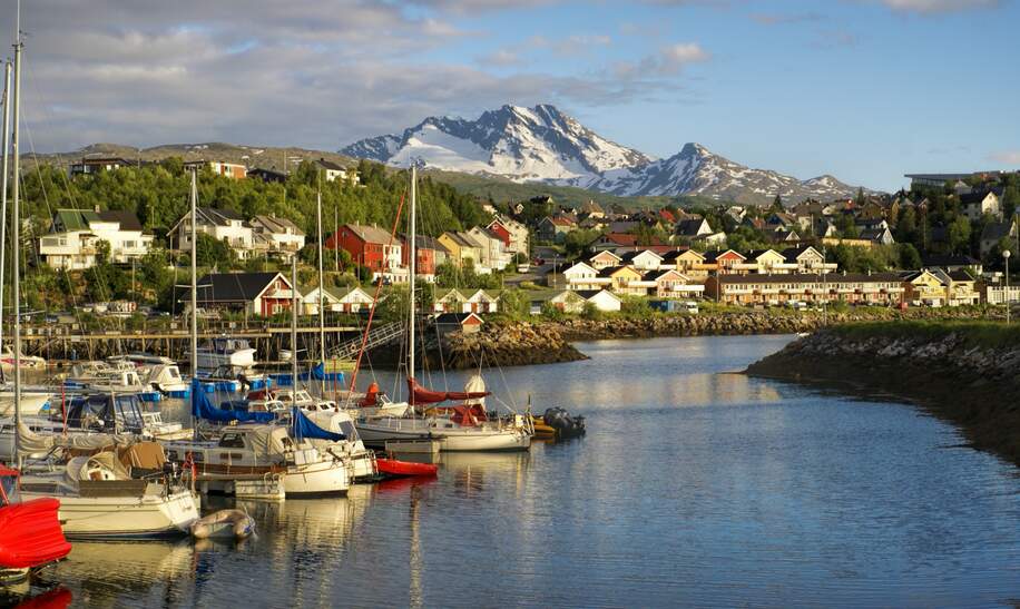 Narvik Hafen mit mehreren Booten, umgeben von Wohnhaeusern und einer Bergkette im Hintergrund unter klarem Himmel. | © gettyimages.com/MisoKnitl
