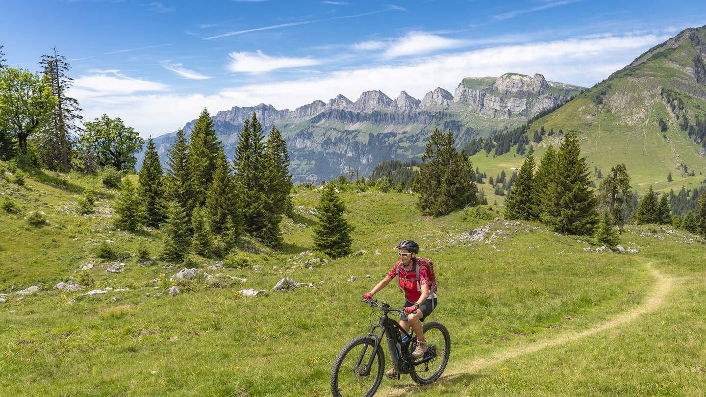 Fahrradfahrerein faehrt bergauf inmitten der Schweizer Alpen bei Sonnenschein und leichten Wolken | © Gettyimages.com/Uwe Moser