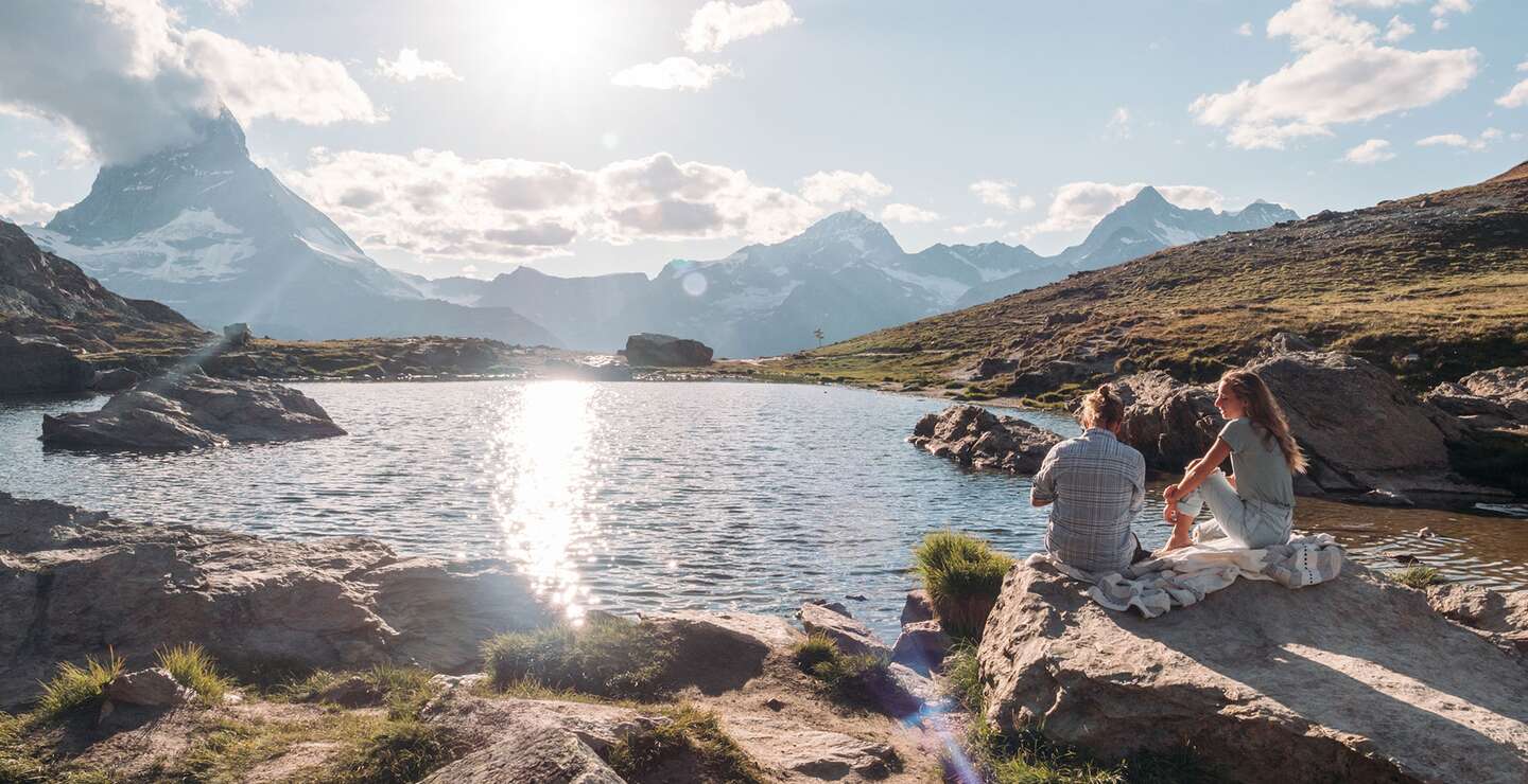Paar geniesst am Seeufer den Sonnenuntergang mit Blick auf das Matterhorn in den Schweizer Alpen | © Gettyimages.com/Mystockimages