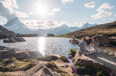 Paar geniesst am Seeufer den Sonnenuntergang mit Blick auf das Matterhorn in den Schweizer Alpen | © Gettyimages.com/Mystockimages