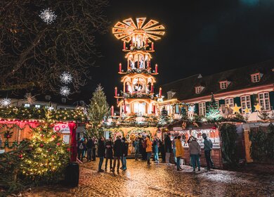 Weihnachtsmarkt bei Nacht mit beleuchteter Holzpyramide und festlich geschmückten Ständen | © Basel Tourismus