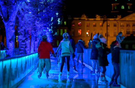 Menschen beim nächtlichen Eislaufen auf einer festlich beleuchteten Außenbahn, umgeben von blau illuminierten Bäumen und städtischer Kulisse mit erleuchteten Gebäuden. | © KTG Karlsruhe Tourismus GmbH, Bruno Kelzer