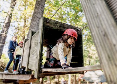 Ein kleines Mädchen klettert gesichert von einer Plattform zur anderen im Hochseilgarten | © Sebastian Becker