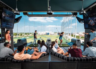 Eine Frau und ein Mann spielen Topgolf während andere zusehen | © Topgolf