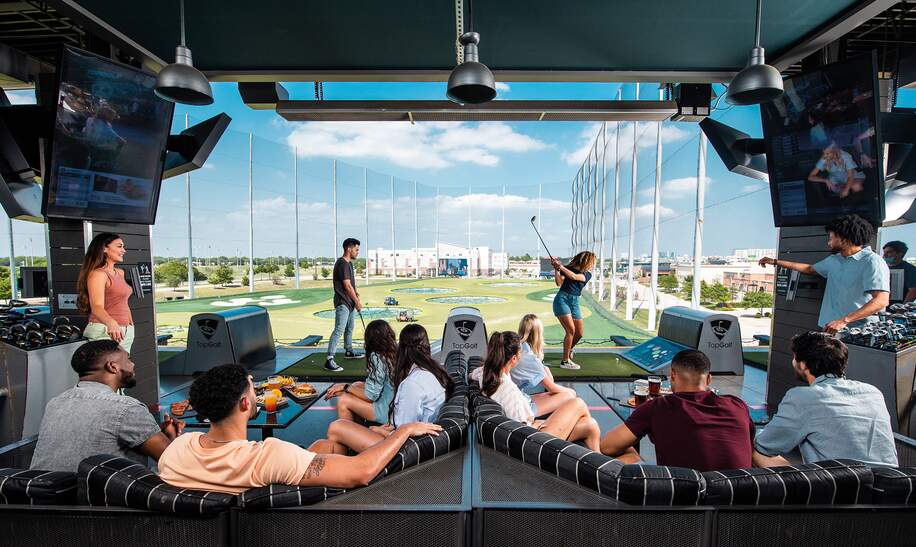 Eine Frau und ein Mann spielen Topgolf während andere zusehen | © Topgolf
