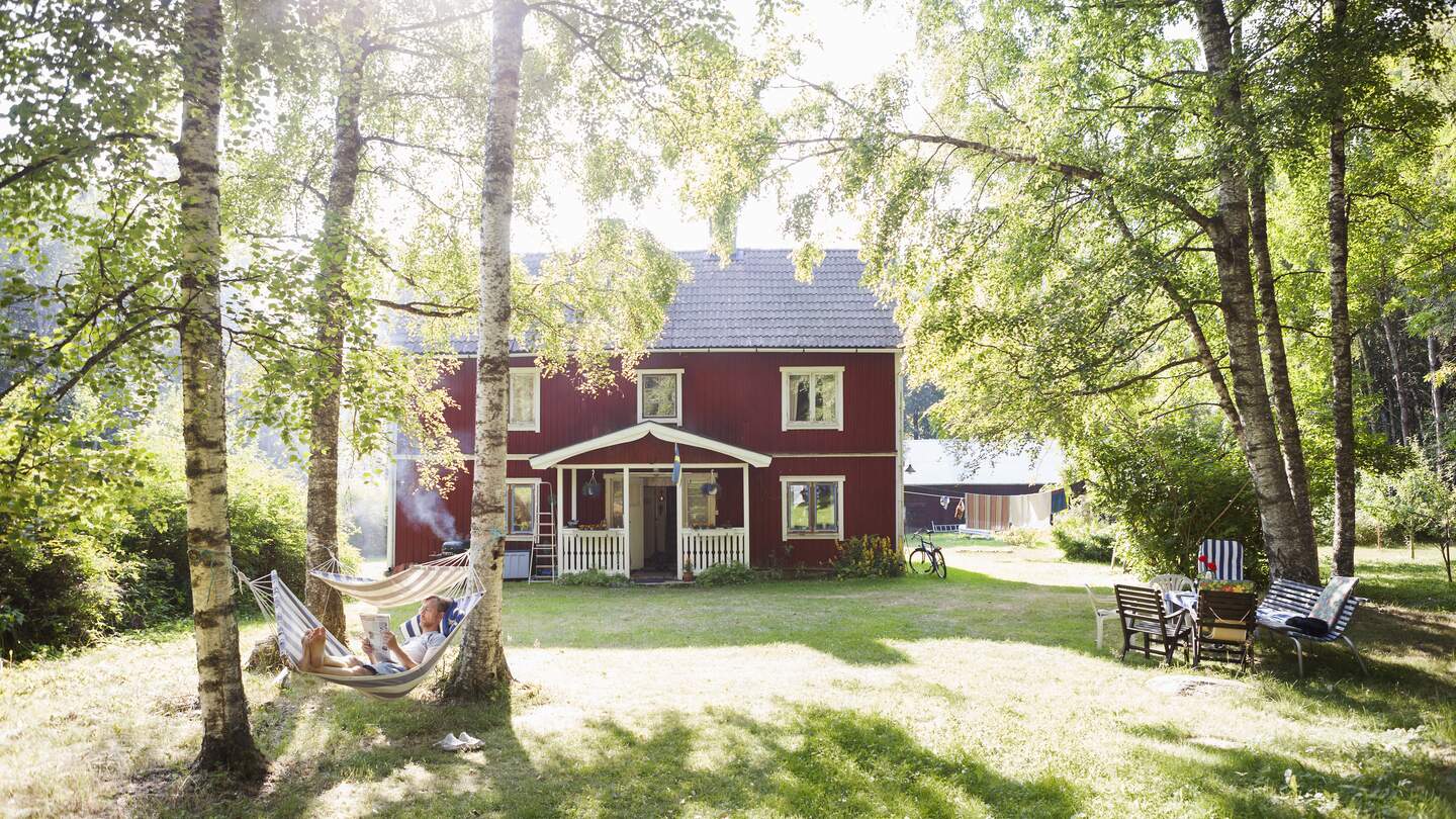 Rotes Ferienhaus inmitten grüner Natur mit Hängematte und Sitzbereich im Garten | © imagebank.sweden.se/Doris Beling