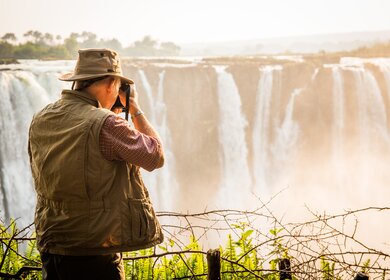 Fotograf bei Sonnenaufgang an den Viktoriafällen in Zimbabwe  während einer Reise im African Explorer | © Gettyimages.com/JanelleLugge