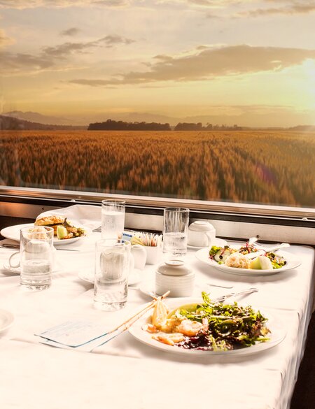 Ein junges Paar sitzt im Restaurantwagen des Zuges The Canadian und schaut auf die untergehende Sonne in der Prärie. | © VIA Rail Canada