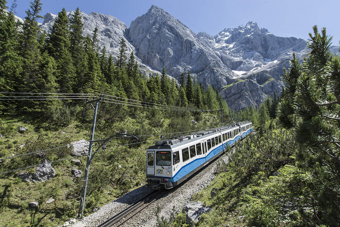 Die historische Zugspitzbahn fährt vor Bergpanorama und umgeben von Tannenwald talwärts von der Zugspitze kommend, Bayern | © Matthias Fend Photography