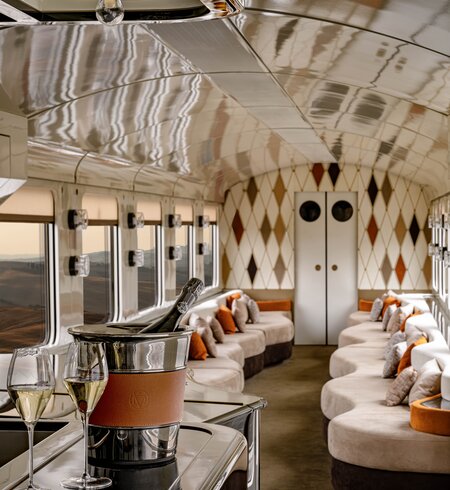Blick in den Barwagen des La Dolce Vita Express, im Vordergrund links der Bartresen mit einer Flasche Cahmpagner im Sektkühler und zwei gefüllten Champagnergläsern | © Orient Express SAS