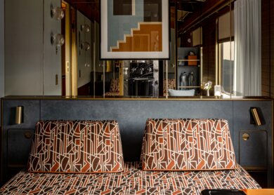 Blick auf das Sofa, in der Tagesansicht mit gemustertem Bezug in Brauntönen, in der Delux Suite des La Dolce Vita Orient Express | © Orient Express SAS