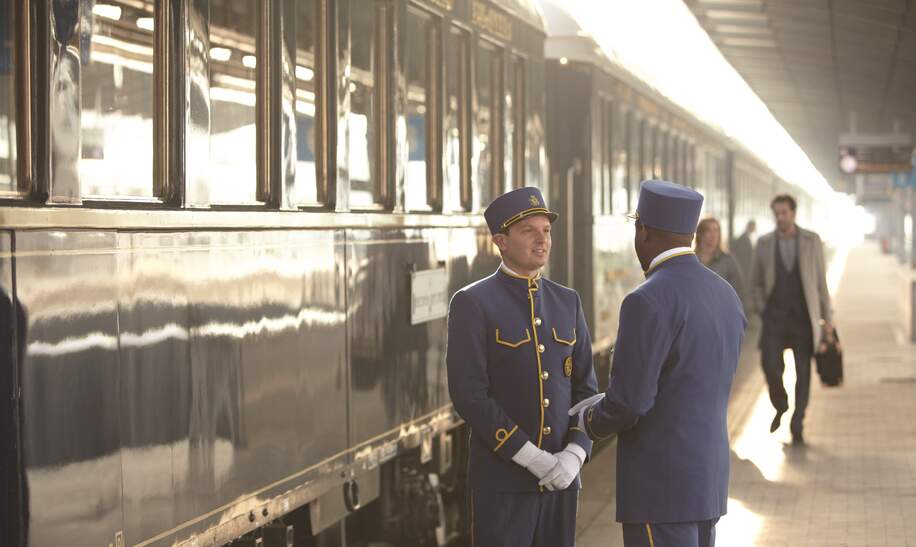 Stewards stehen auf dem Bahnsteig vor dem Venice Simplon Orient Express. Passagiere laufen vorbei. | ©  Matt Hind