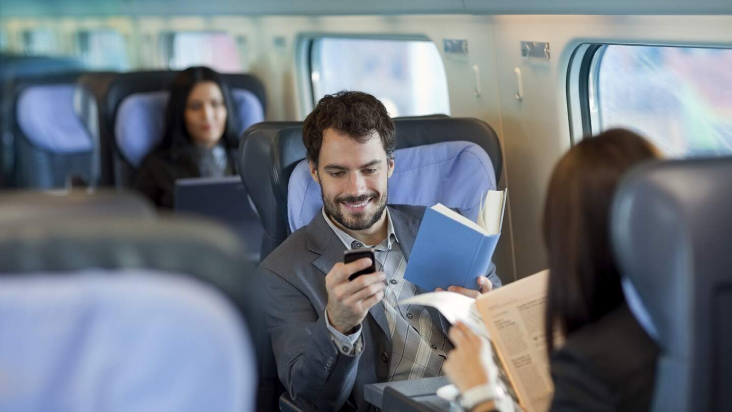 Innere eines Zugabteils, in dem Passagiere verschiedene Aktivitäten ausüben: Eine Person liest ein Buch, eine andere nutzt ein Smartphone und eine dritte Person liest eine Zeitung.  | ©  Deutsche Bahn AG
