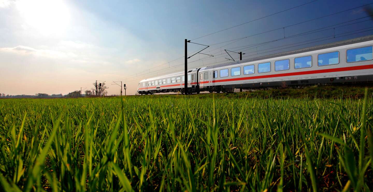 Ein  ICE fährt durch ein grünes Feld unter klarem Himmel, was die Dynamik moderner Transportmittel in einer natürlichen Umgebung zeigt. | ©  Deutsche Bahn AG
