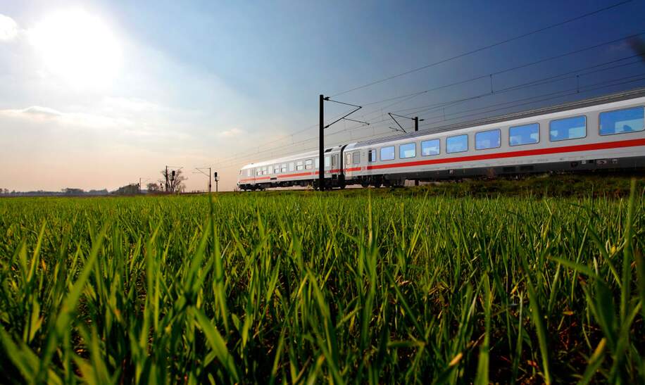 Ein  ICE fährt durch ein grünes Feld unter klarem Himmel, was die Dynamik moderner Transportmittel in einer natürlichen Umgebung zeigt. | ©  Deutsche Bahn AG