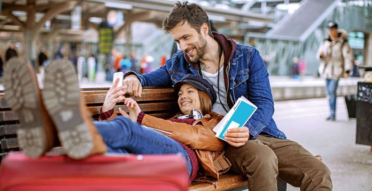Ein Paar schaut auf das Handy waehrend es auf der Bank wartet  | © gettyimages.com/Geber86