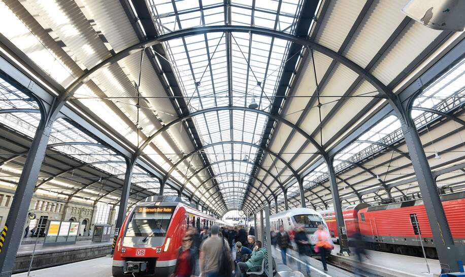 einen belebten Bahnhof mit einem roten Zug auf der linken Seite und einem weiteren Zug auf der rechten Seite | © Deutsche Bahn AG/Oliver Lang
