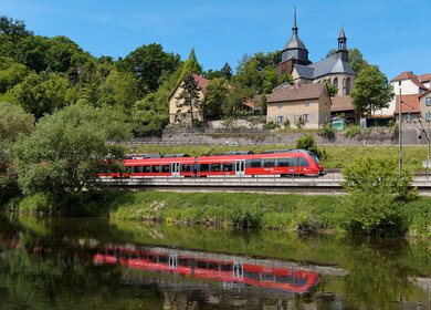 Ein roter DB-Zug faehrt durch einen besiedelten Ort | © Deutsche Bahn AG/Frank Barteld