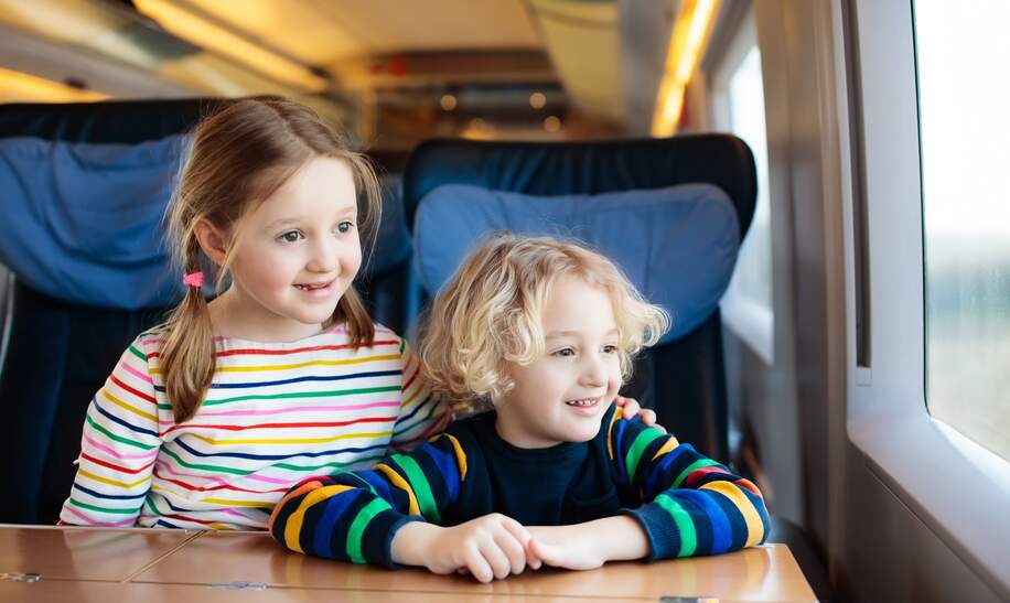 Zwei Kinder schauen aus dem Fenster währen sie mit der Bahn verreisen | © Gettyimages.com/FamVeld