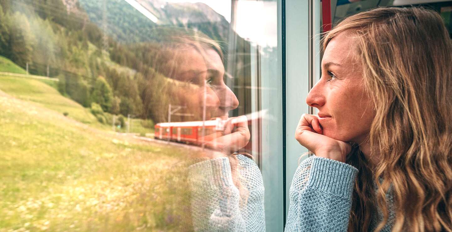 Frau, die mit dem Zug aus dem Fenster schaut und die landschaftlich vorbeifahrende Landschaft geniesst | © Gettyimages.com/Mystockimgaes