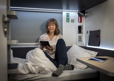 Eine Frau sitzt auf dem Bett der Kategorie comfort im Schlafwagen des ÖBB Nightjets der neuen Generation | © ÖBB/Harald Eisenberger