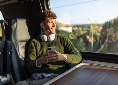 Reisender im Zug mit Kopfhörern schaut aus dem Fenster | © GettyImages.com/Riska