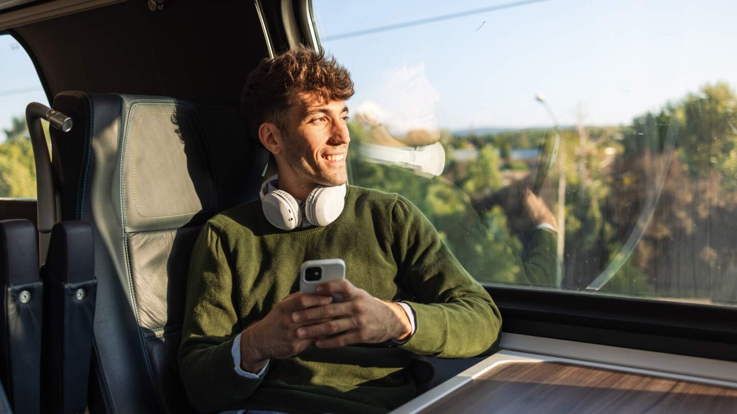 Reisender im Zug mit Kopfhörern schaut aus dem Fenster | © GettyImages.com/Riska