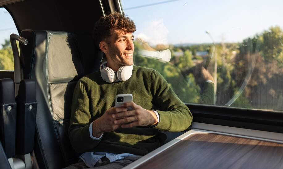 Reisender im Zug mit Kopfhörern schaut aus dem Fenster | © GettyImages.com/Riska