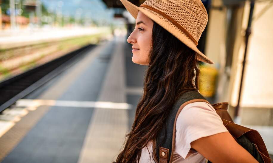 Eine Frau steht am Bahnhof, um ihre Staedtereise mit dem Zug zu beginnen, und freut sich auf die bevorstehende Entdeckung neuer Staedte. | © Gettyimages.com/MStudioImages