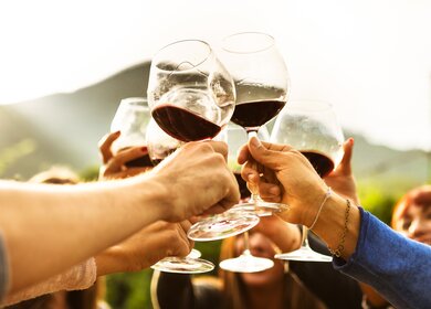 Haende von Männern und Frauen die in der Mitte zusammenkommen und mit Rotwein anstossen | © Gettyimages.com/franckreporter
