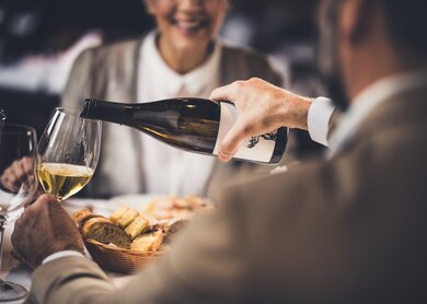 Nahaufnahme eines unkenntlichen Mannes, der seiner Frau waehrend des Mittagessens in einem Restaurant Wein einschenkt. | © Gettyimages.com/skynesher