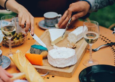 Freunde genießen einen typisch französischen Brunch mit Wein, Brie-Käse, Blauschimmelkäse, Weißwein und Baguettes in Paris. | © Gettyimages.com/lechatnoir