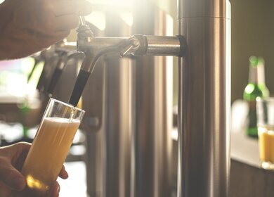 Nahaufnahme der Hand eines Wirtes, der Bier in einer Bar zapft | © Gettyimages.com/pxel66