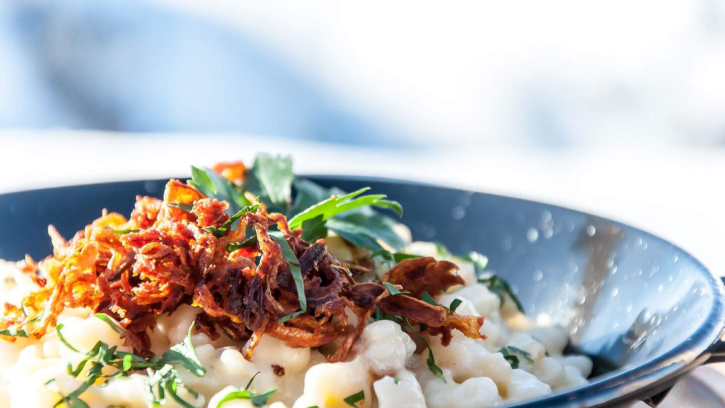 Allgaeuer Kaesspatzen mit Roestszwiebeln lecker angerichtet in dunkelblauer Schale mit gruenen Kraeutern dekoriert | © Gettyimages.com/Max2611