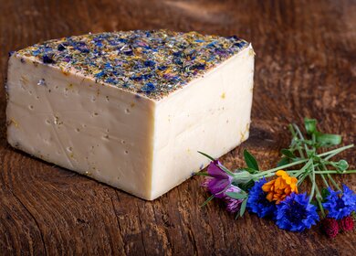 Bergkaese mit getrockneten Blumen auf einem Holzbrett | © Gettyimages.com/bernjuer