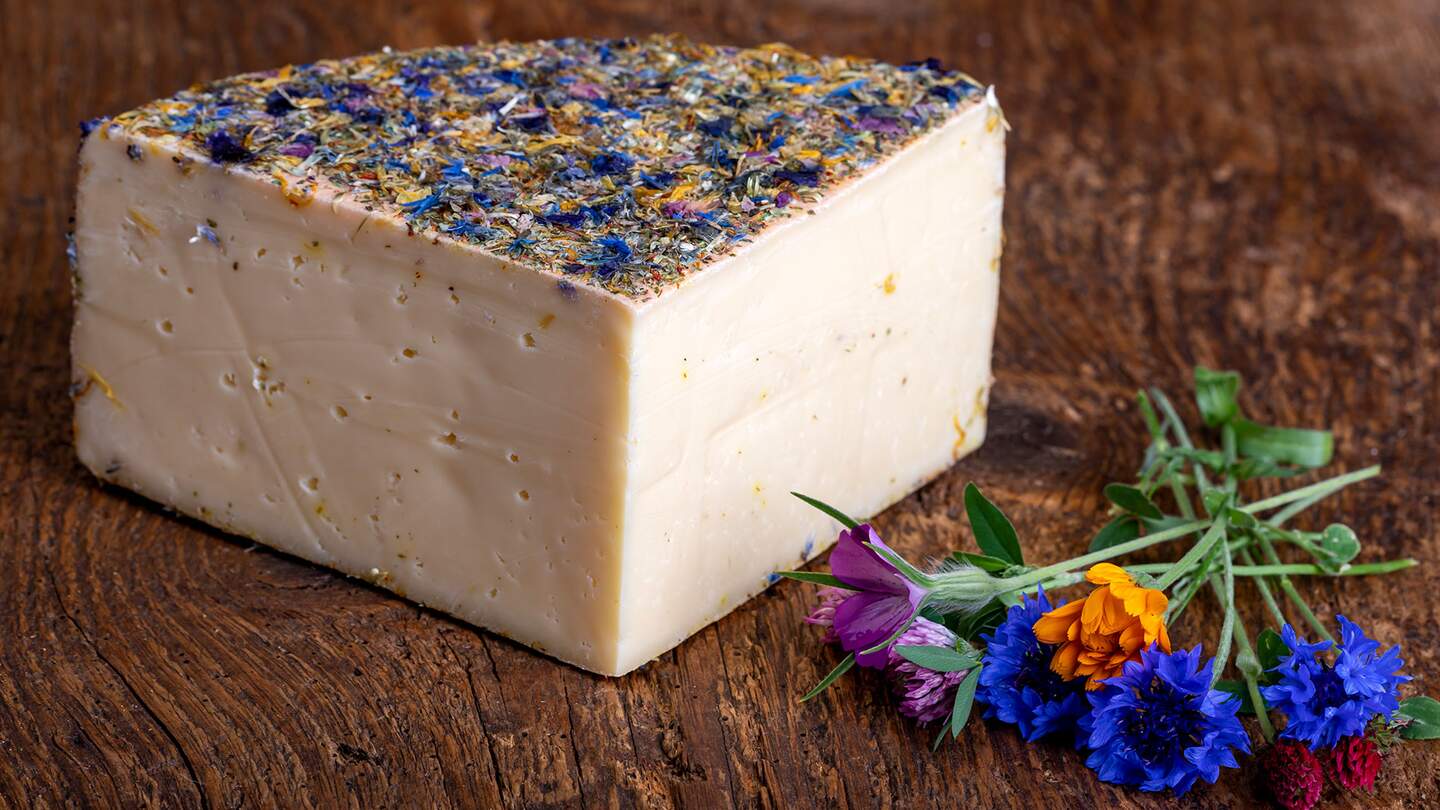 Bergkaese mit getrockneten Blumen auf einem Holzbrett | © Gettyimages.com/bernjuer