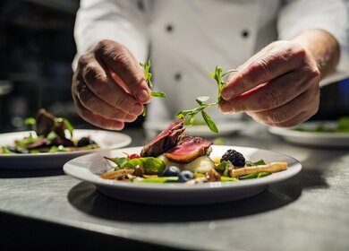 Koch dekoriert Essen. Das Gericht ist, gebratene rosa Entenbrust auf ein Bett aus Pastinakenpueree mit saisonalem Herbstgemuese und Beeren. | © Gettyimages.com/ClarkandCompany