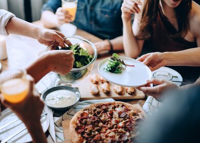 Nahaufnahme einer jungen Gruppe froehlicher Freunde, die Spass daran haben, zusammen zu genießen, Essen ueber den Esstisch auf der Party zu verteilen und zu teilen | © Gettyimages.com/AsiaVision