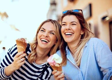 Zwei junge Frauen mit Eis in der Hand und lachen froehlich | © Gettyimages.com/djiledesign