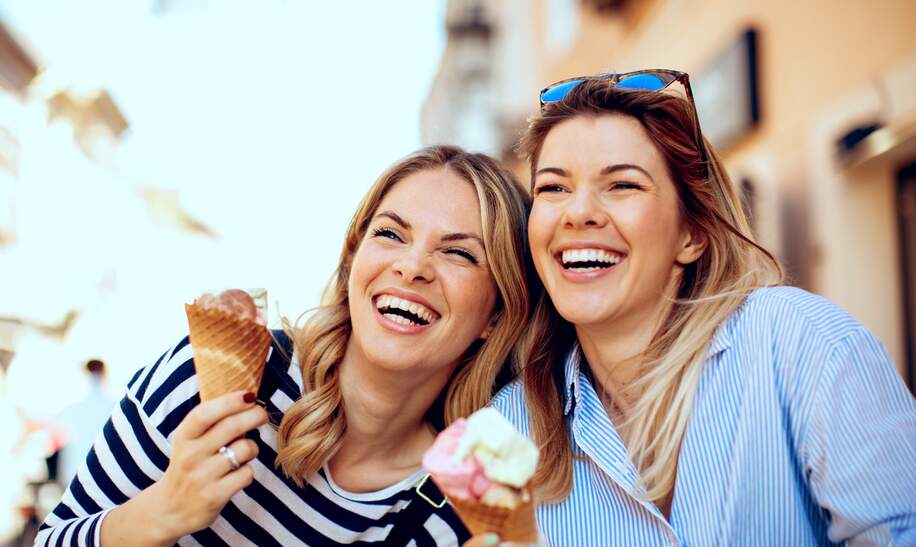 Zwei junge Frauen mit Eis in der Hand und lachen froehlich | © Gettyimages.com/djiledesign