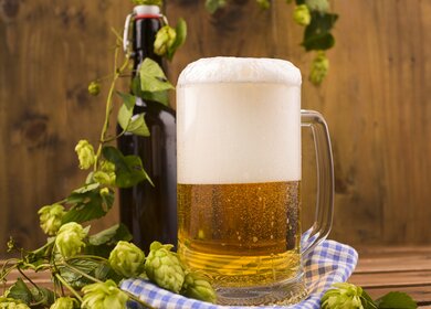 Ein Glas Bier aus nächster Nähe auf einem hoelzernen Hintergrund mit Flasche im Hintergrund | © Gettyimages.com/marinabakush
