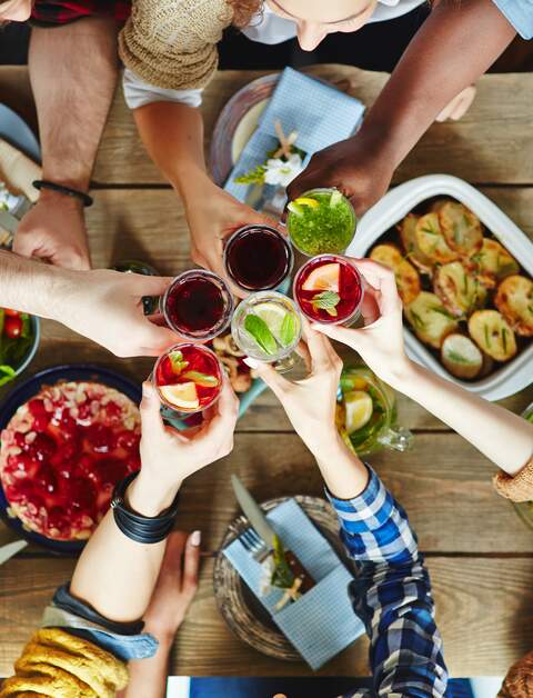 Blick von oben auf Freunde, die mit ihren Limonaden an einem gedeckten Tisch anstossen | © Gettyimages.com/shironosov