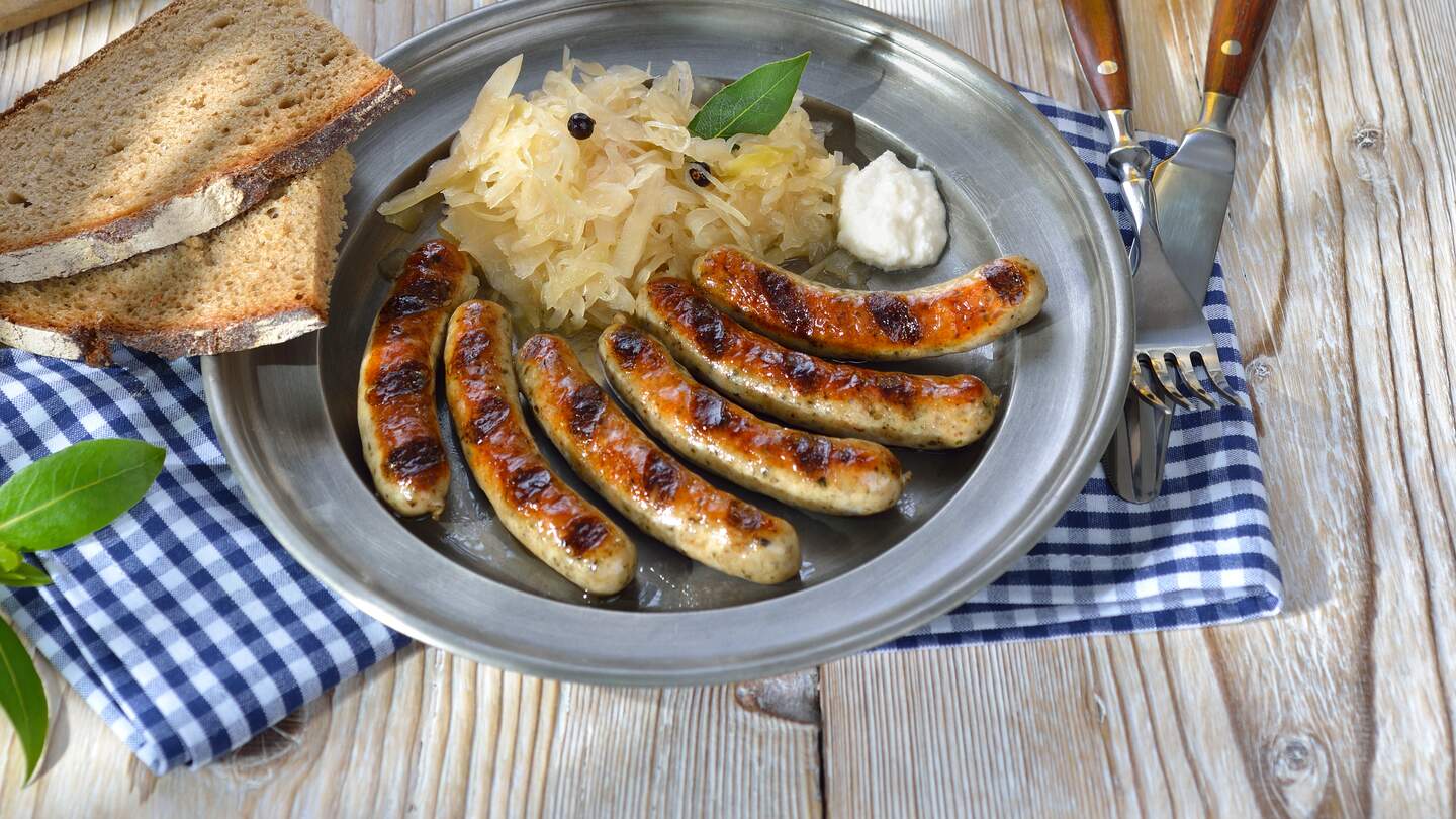 Nuernberger Bratwuerste mit Sauerkraut und Meerrettich traditionell serviert auf einem Zinnteller mit herzhaftem Bauernbrot und einem Humpen kaltem Muenchner Bier | © Gettyimages.com/kabVisio