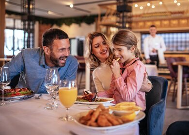 Eine Familie mit einem weiblichen Kind isst in einem Restaurant zu Mittag | © Gettyimages.com/zeljkosantrac