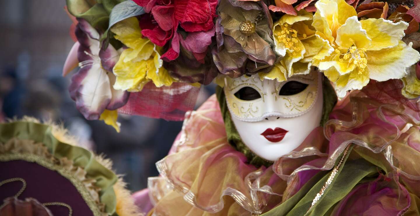 Frau in venezianischer Karnevals Verkleidung, mit Maske, pompoesem Blumenkopfschmuck und vielen Rueschen | © GettyImages.com/t-lorien