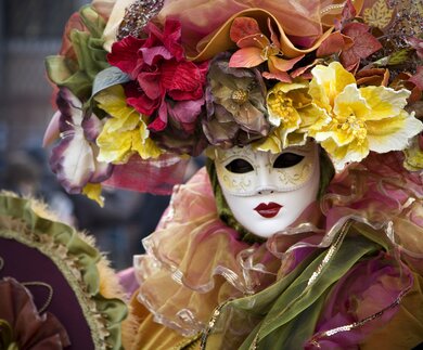 Frau in venezianischer Karnevals Verkleidung, mit Maske, pompoesem Blumenkopfschmuck und vielen Rueschen | © GettyImages.com/t-lorien
