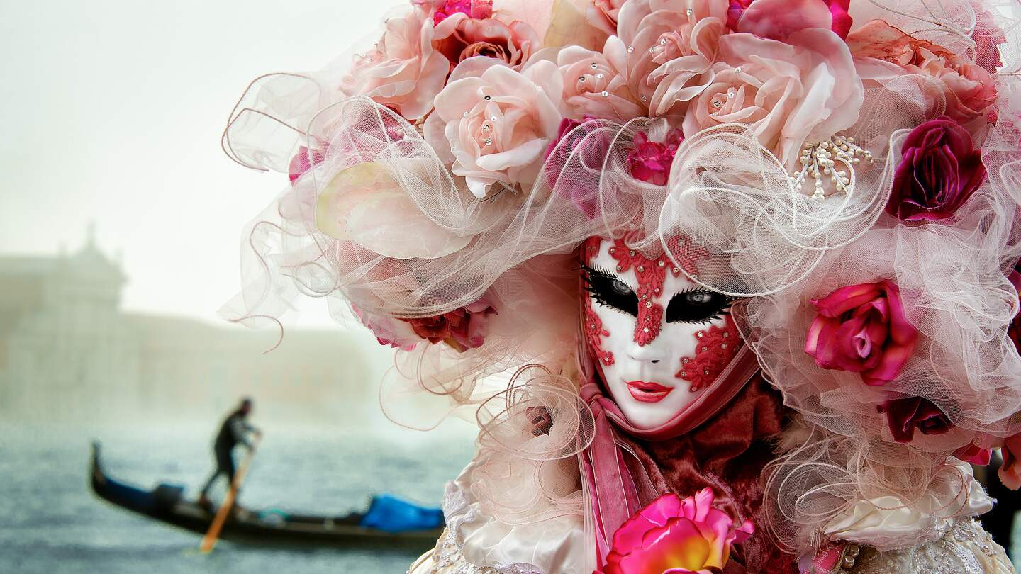 Eine typische kunstvolle Maske des Venezianischen Karnevals in Italien, im Hintergrund eine Gondel auf einem Kanal von Venedig | © GettyImages.com/shahramazizi